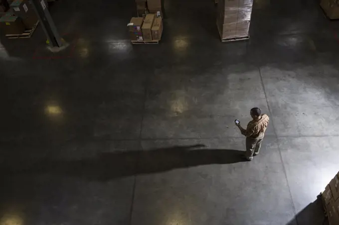 A storeroom manager seen from above in a darkened warehouse, looking at his phone.