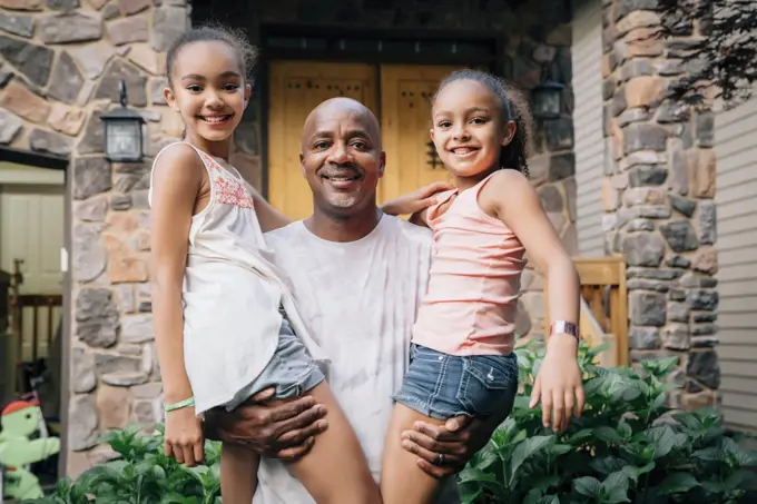 Portrait of happy dad hugging daughters in front of house