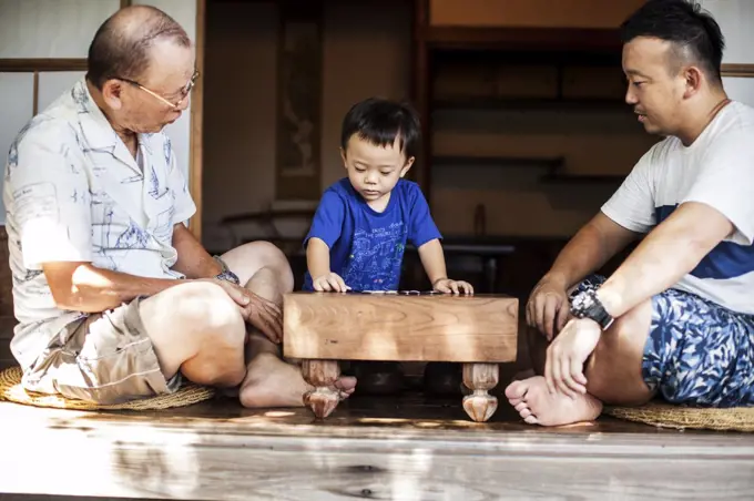 Two Japanese men and little boy sitting on floor on porch of traditional Japanese house, playing Go.