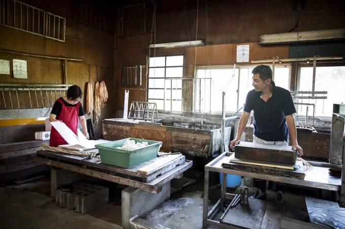 Two people, man and woman making traditional Washi paper. Trays of pulp and wooden frames and drying racks. 