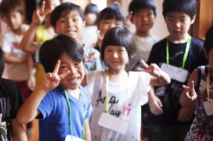 Group of smiling children in a Japanese preschool, making peace sign, looking at camera.