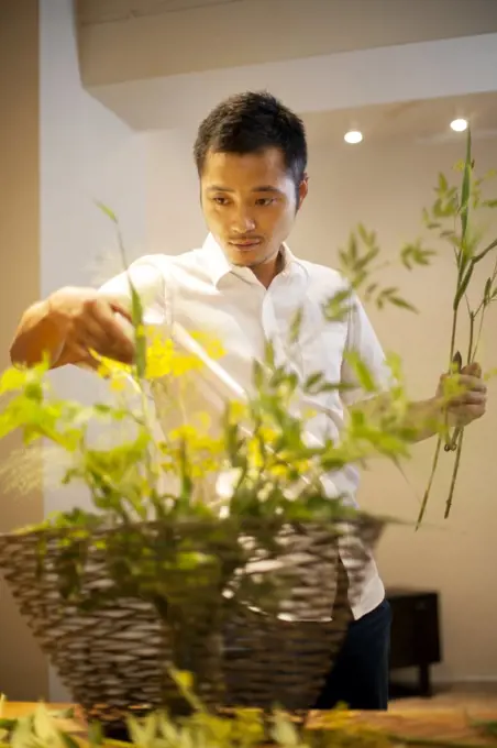Japanese man standing in flower gallery, working on Ikebana arrangement.