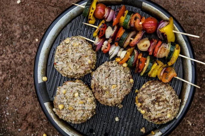 Food on a barbeque, vegetable kebabs and home made burgers, cooking outdoors.