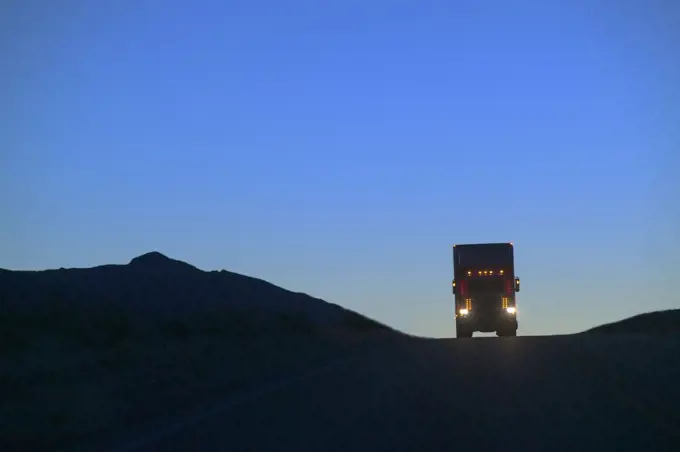 A Class 8 truck silhouetted while coming over a hill on the highway.