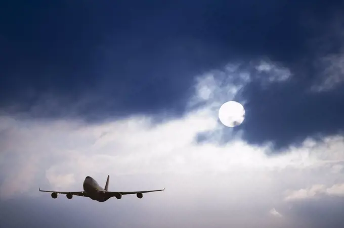 An aircraft in the air, silhouette against a dark blue sky with white cloud.