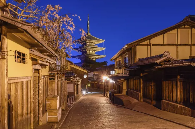 Traditional houses lining a narrow street with a pagoda in the distance, Higashiyama at night, Kyoto, Japan.