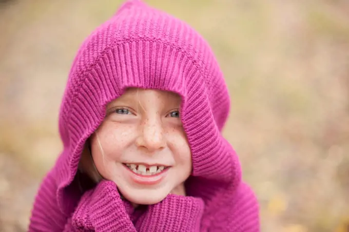 A girl in a magenta hooded sweater, with the hood covering her head, and hands hidden in her cuffs. Keeping warm.