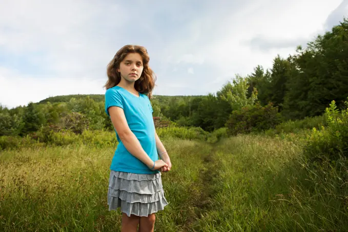A young girl standing by a path through the long grass in a field. New York state, USA. 6/26/2012