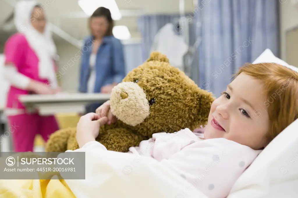 Girl hugging teddy bear in hospital bed