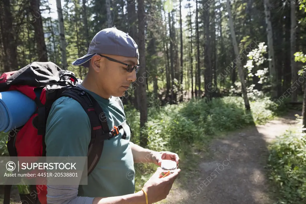 Backpacker checking compass on trail in woods