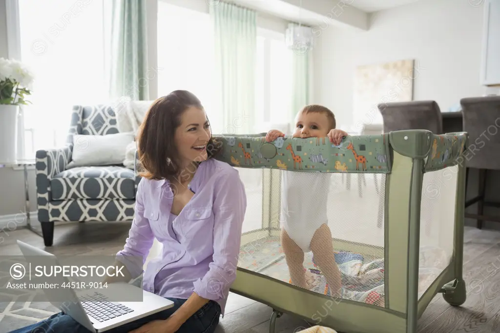 Mother sitting by baby crib with laptop