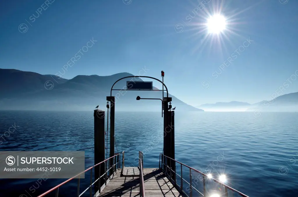 Pier on Alpine Lake Maggiore with Mountain and Sunbeam in Ascona, Switzerland.