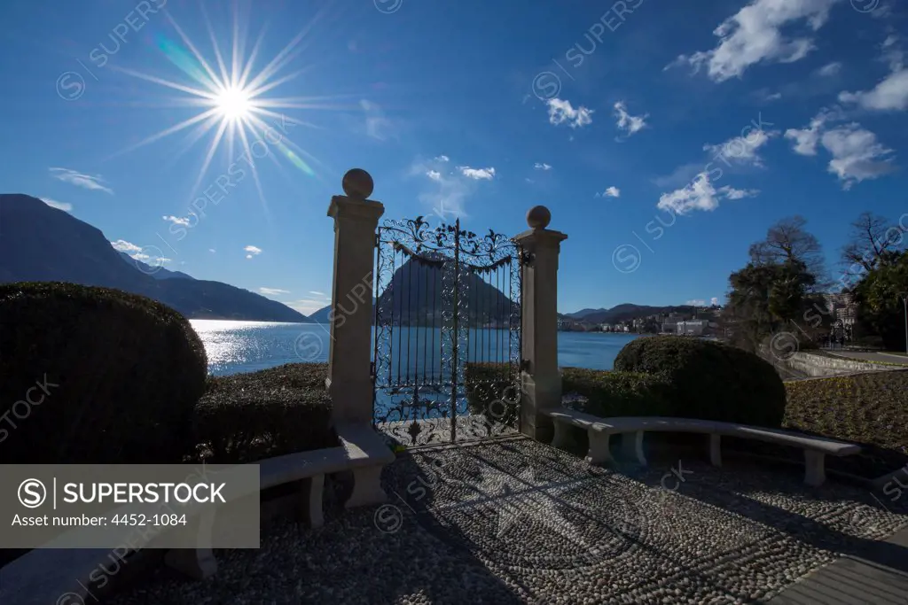 Gate on the Waterfront with Sunbeam and Alpine Lake Lugano with Mountain in Ticino, Switzerland.