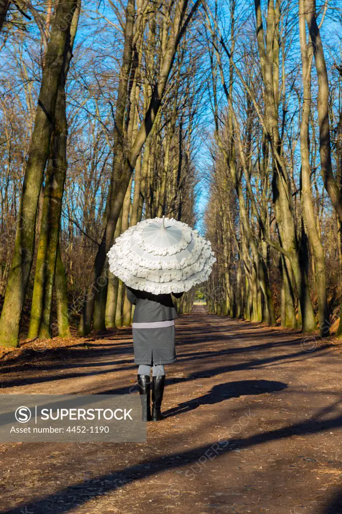 Woman with an Umbrella in a Forest Road with Bare Tree in a Sunny Say in Lombrady, Italy.