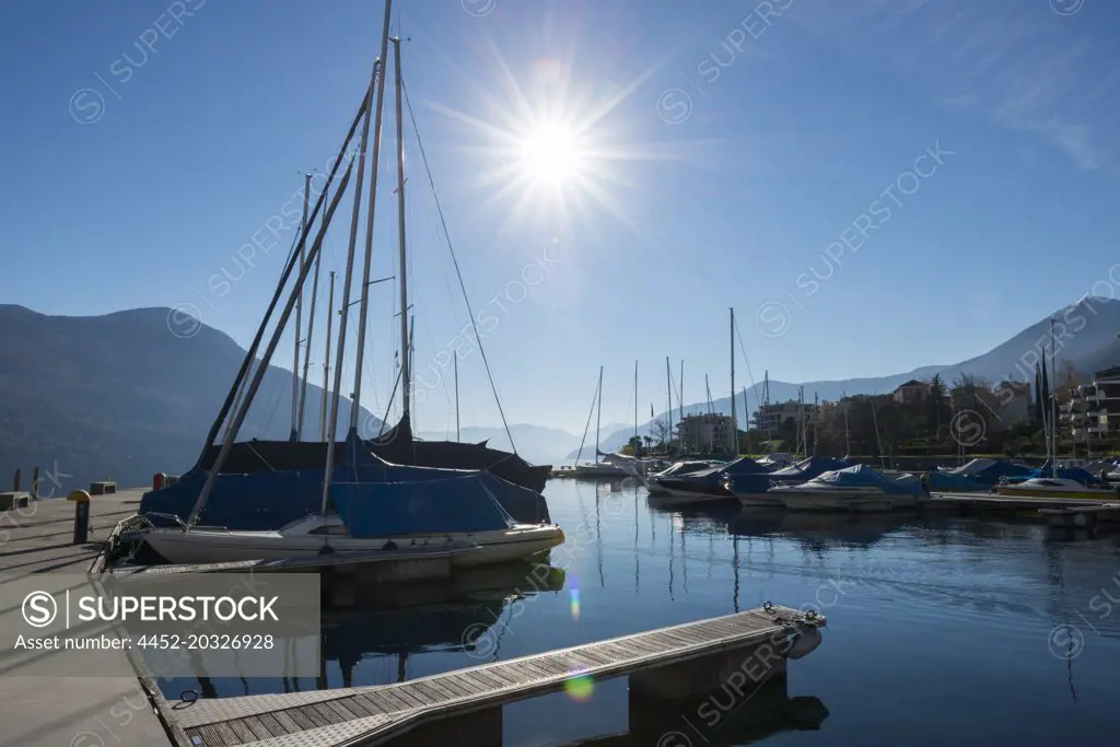 Port with Nautical Vessel on Alpine lake Maggiore with Mountain and Sunbeam in Brissago, Switzerland.