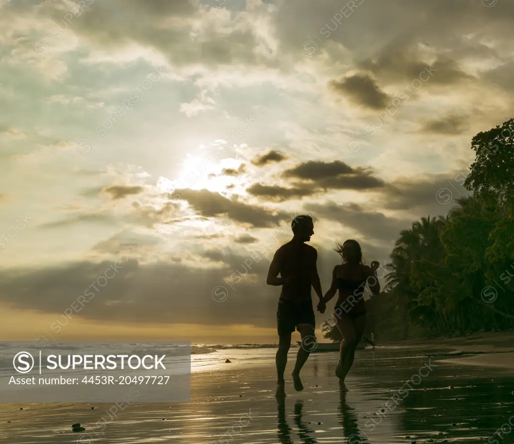 Couple running on tropical beach at sunset