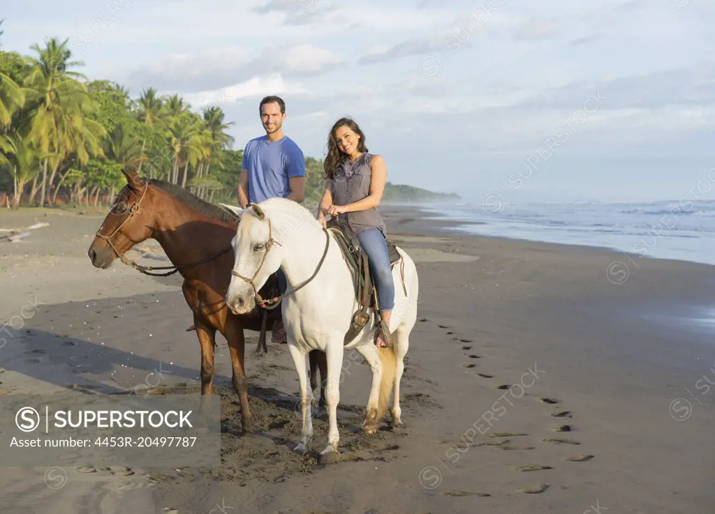Couple riding horses on tropical beach