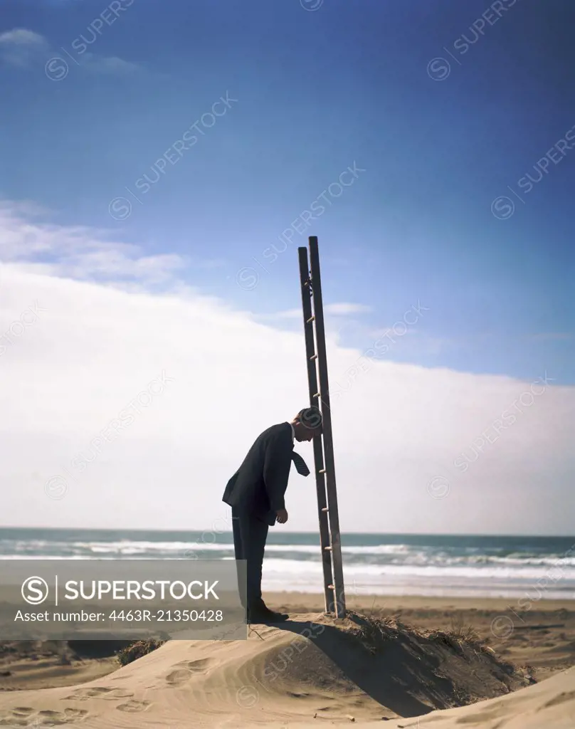 Man standing with head against ladder on a beach
