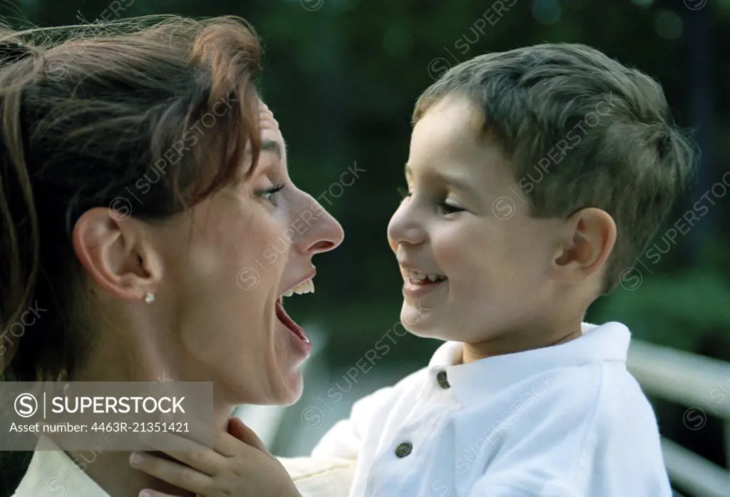 Mid-adult woman joking with her young son while holding him.