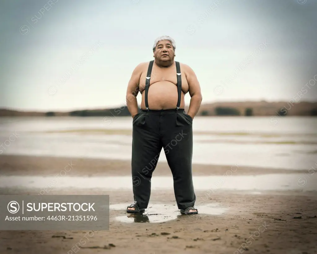 Portrait of a man standing on a beach wearing suspenders.