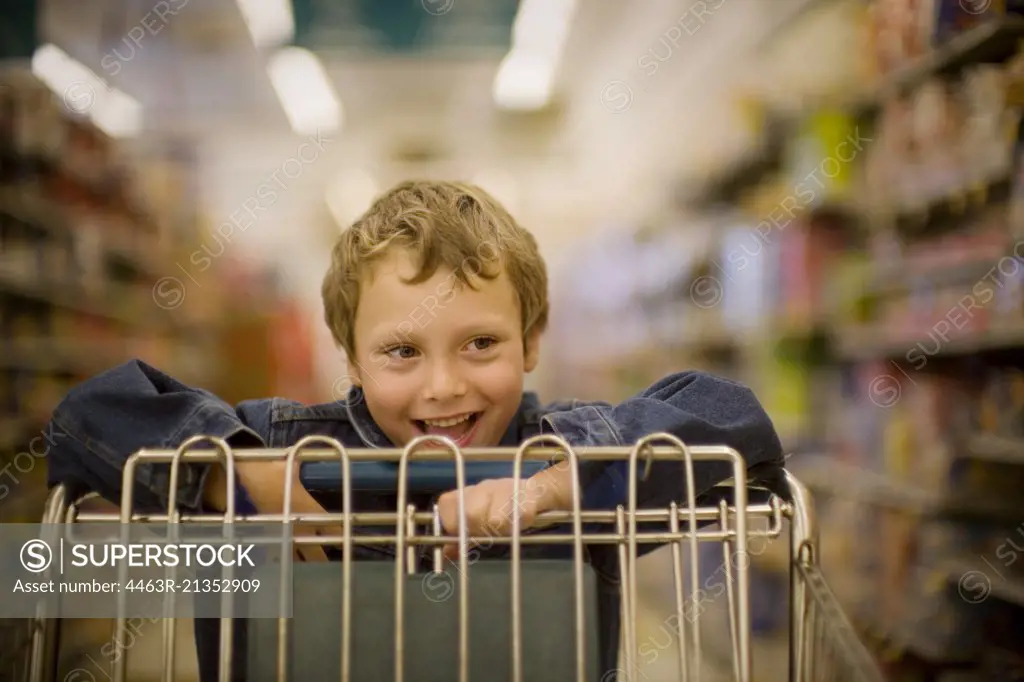 Smiling young boy pushing a trolley at a supermarket.