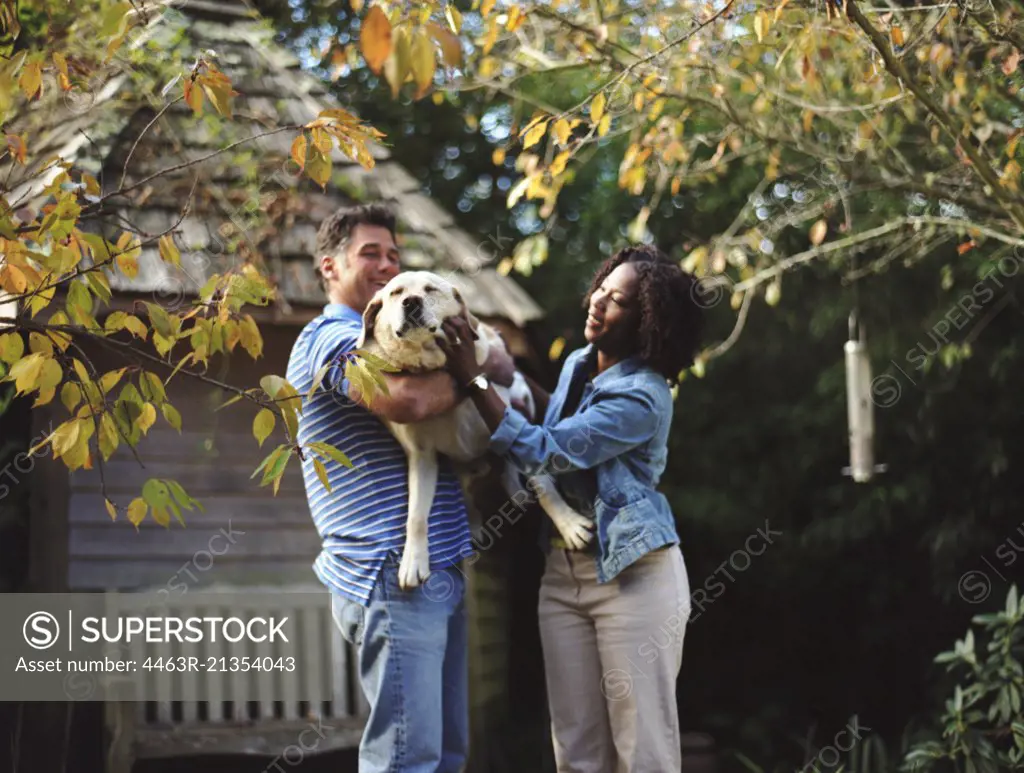 Happy mid-adult couple patting their dog in the back yard of their home.
