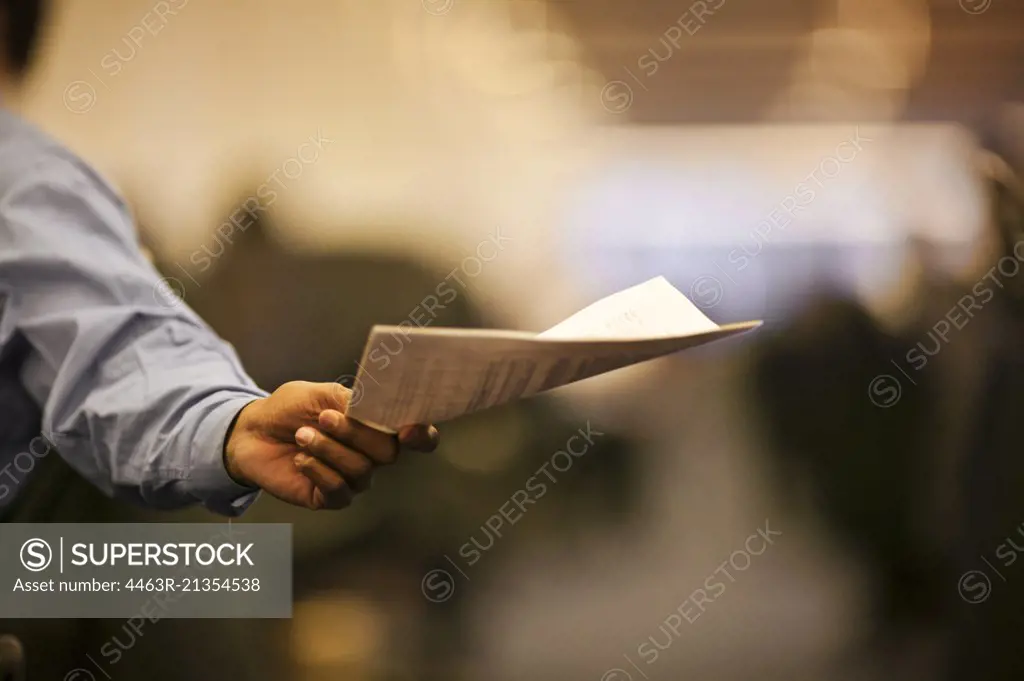 Businessman holds out documents for someone to take.