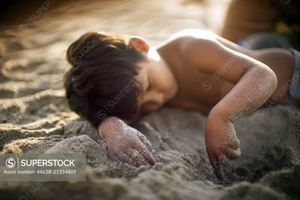 A boy lying on the beach plays with the sand