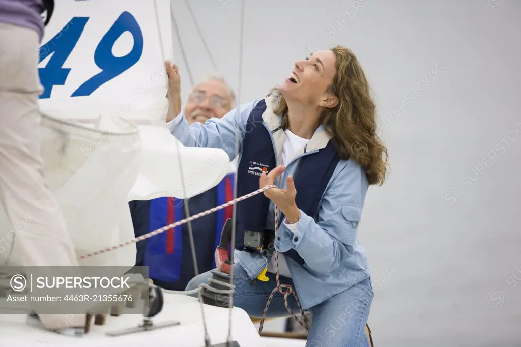 Mature adult woman lowering the sail of a boat while her husband looks on.