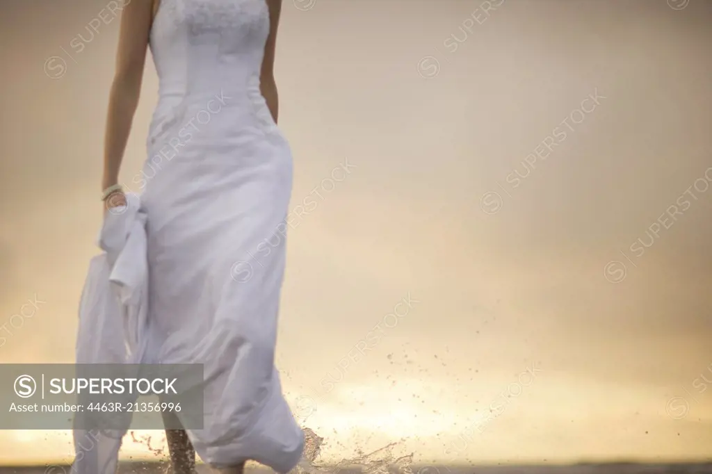 Mid adult woman walking in a wedding dress at sunset.