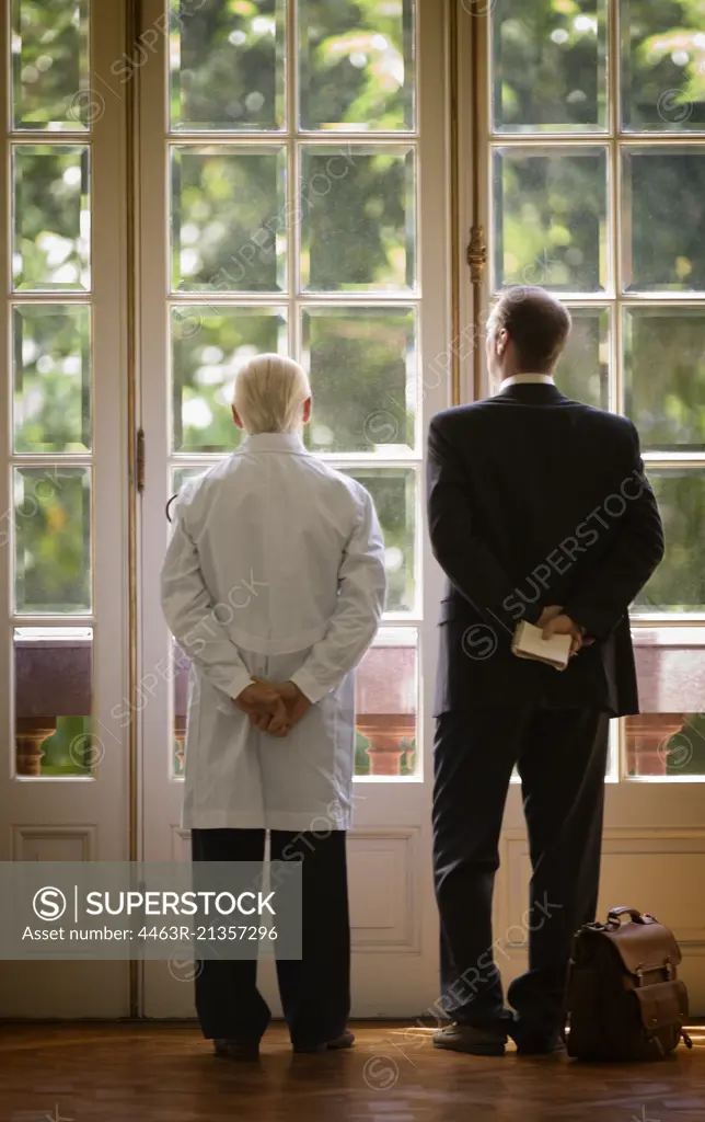 Rear view of two men standing against a glass door.