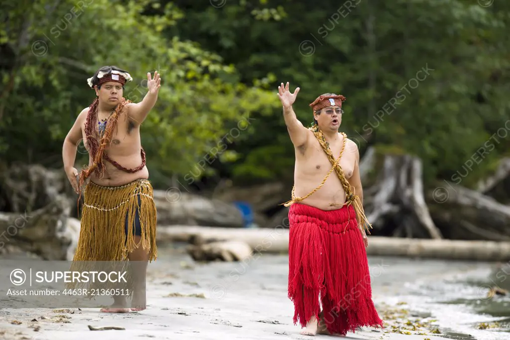 Mid-adult man and a young adult man wearing traditional dress performing a traditional greeting beside a lake.