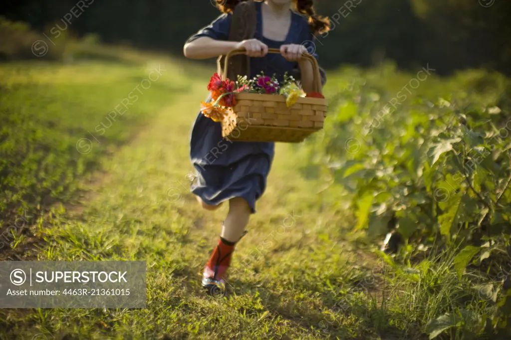 Basket of flowers being held by a young girl running through a field.