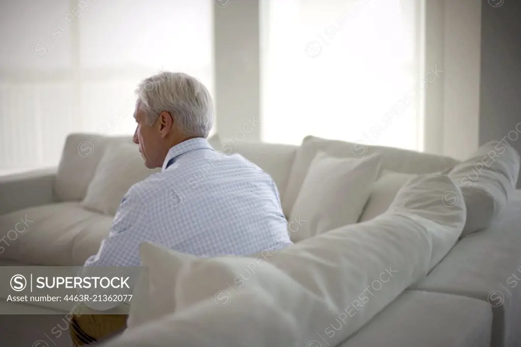 Mature man sitting alone on a couch in his living room.