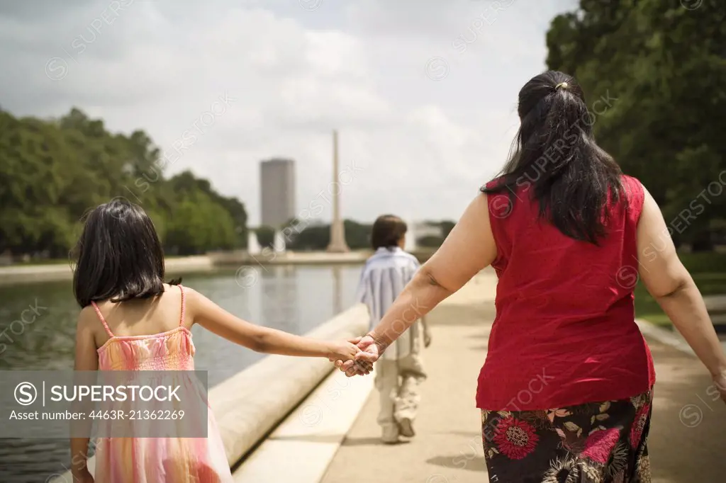 Mother and daughter holding hands as they walk next to a canal.