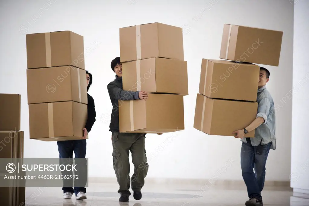 Three young adult men carrying boxes.