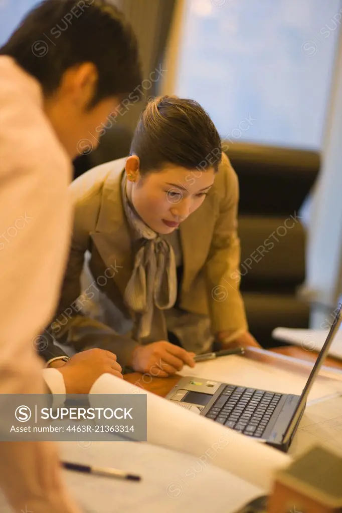 Young adult business woman looking at a laptop with a male colleague in an office.