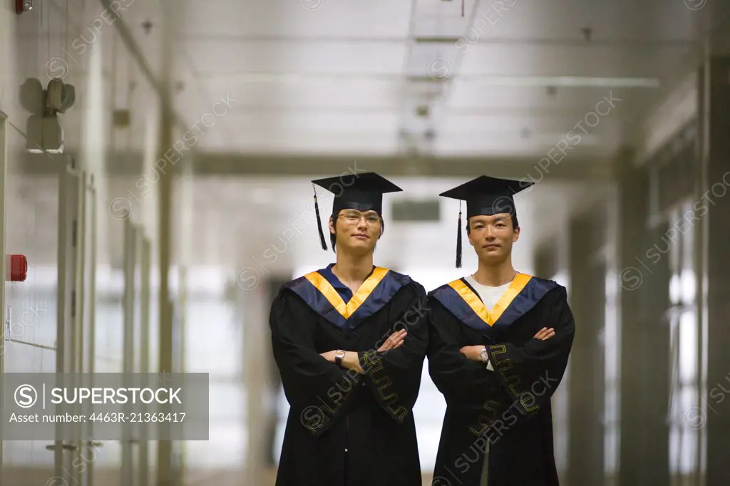 Two teenage boys with folded arms wearing graduation regalia.