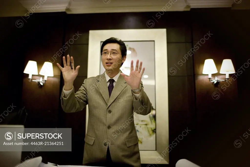 Young adult businessman standing with hands up in a boardroom.