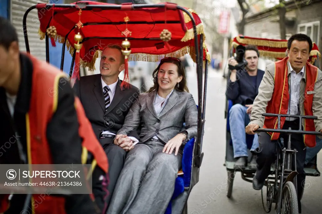Smiling tourists riding in pedicabs along a city street.