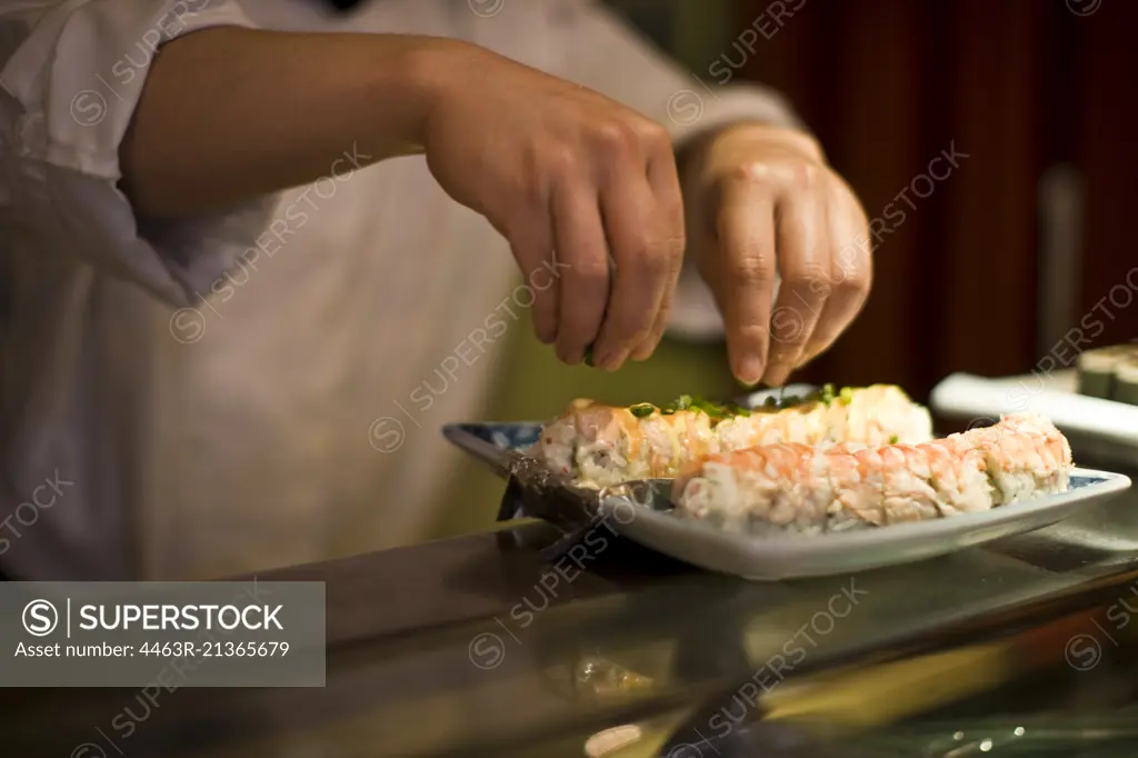 Garnish being sprinkled on a plate of sushi.