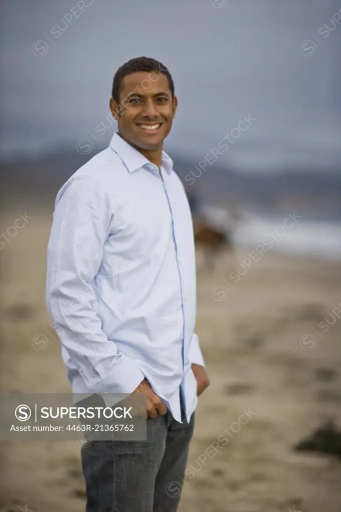 Portrait of a smiling man standing on a remote beach with hands in his pockets.