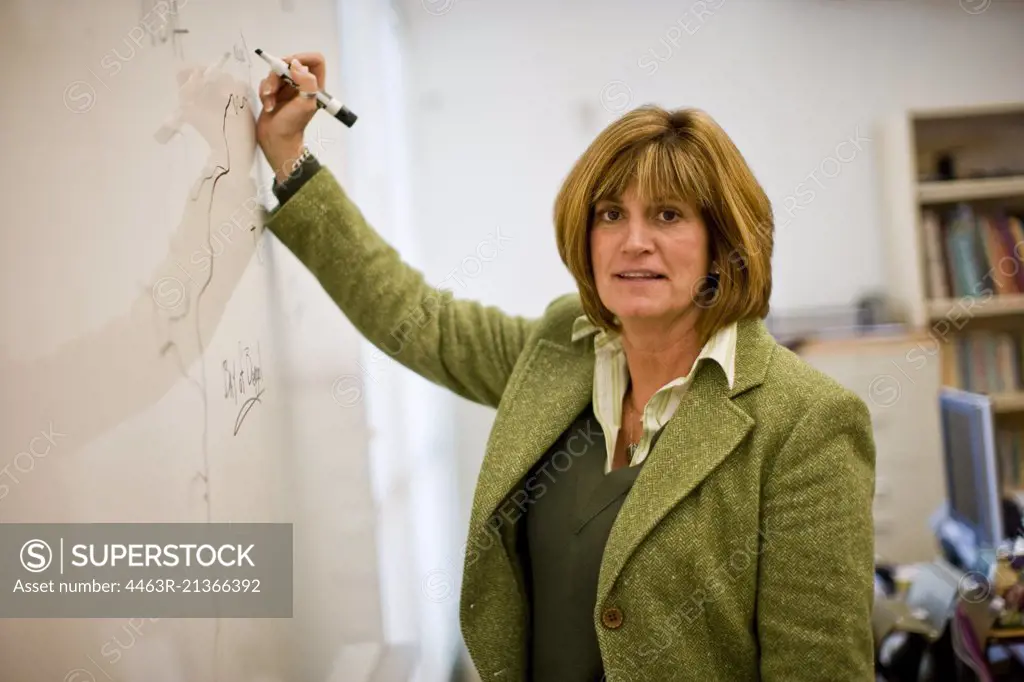 Portrait of a mature female teacher writing on a board standing in a classroom.