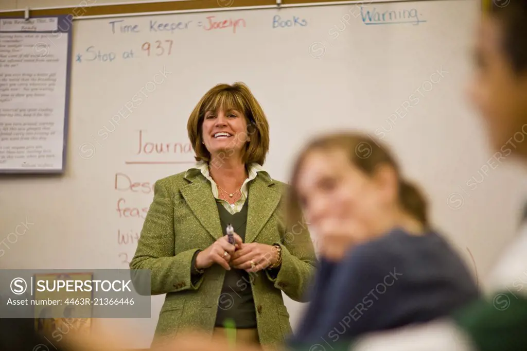 Smiling mid-adult teacher standing at the front of the class in a classroom.