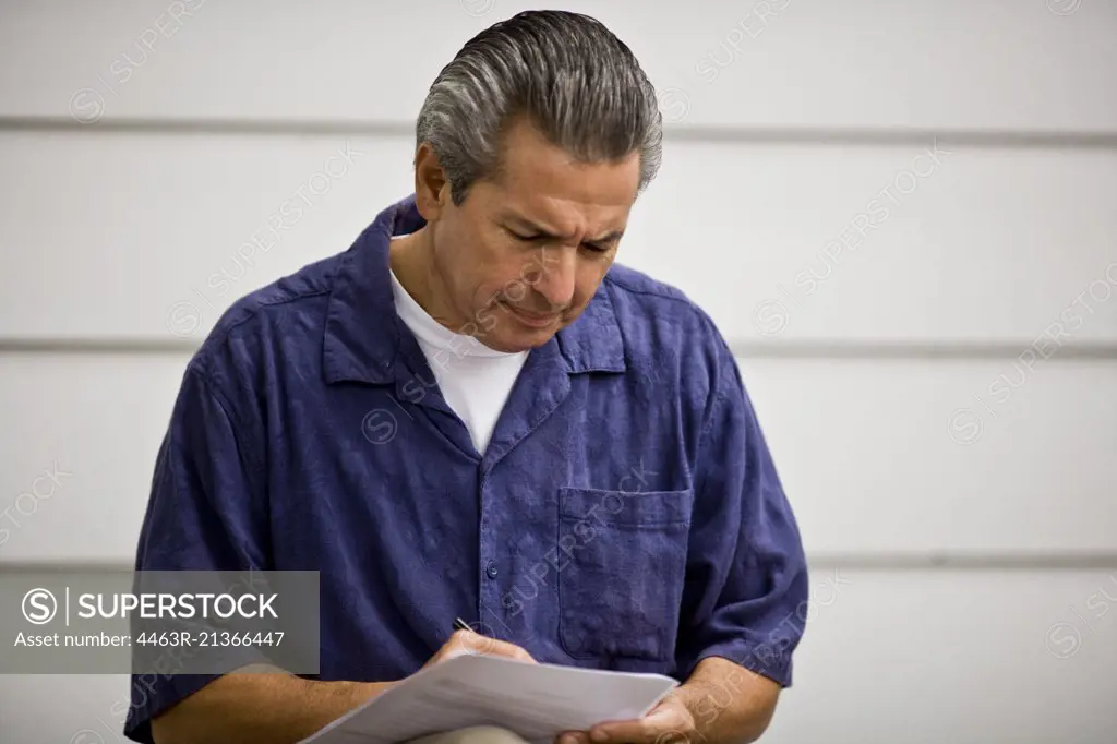Mature man frowning while looking down and writing on a piece of paper.
