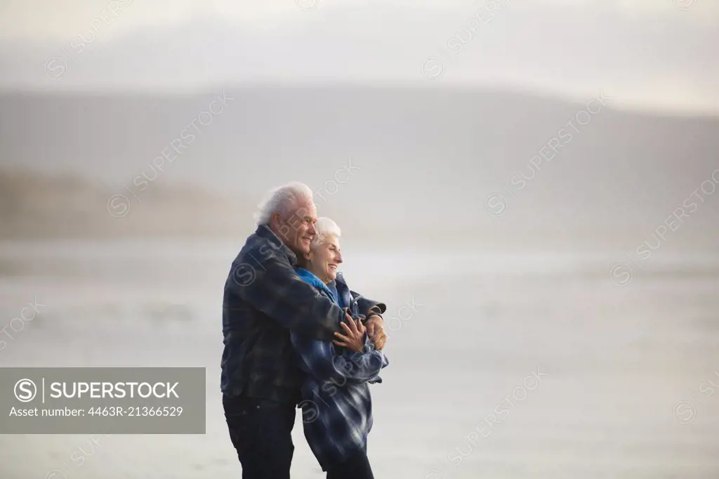 Happy mature couple standing with their arms around each other on a remote beach.