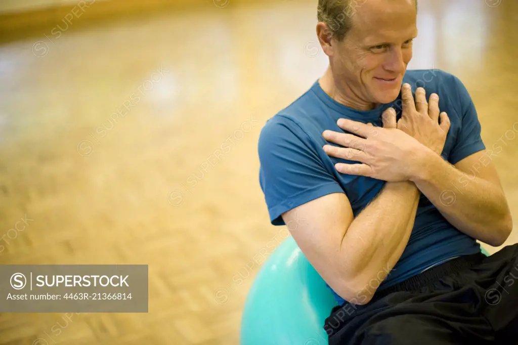 Smiling mature man sitting on an exercise ball with his  hands crossed on his chest.