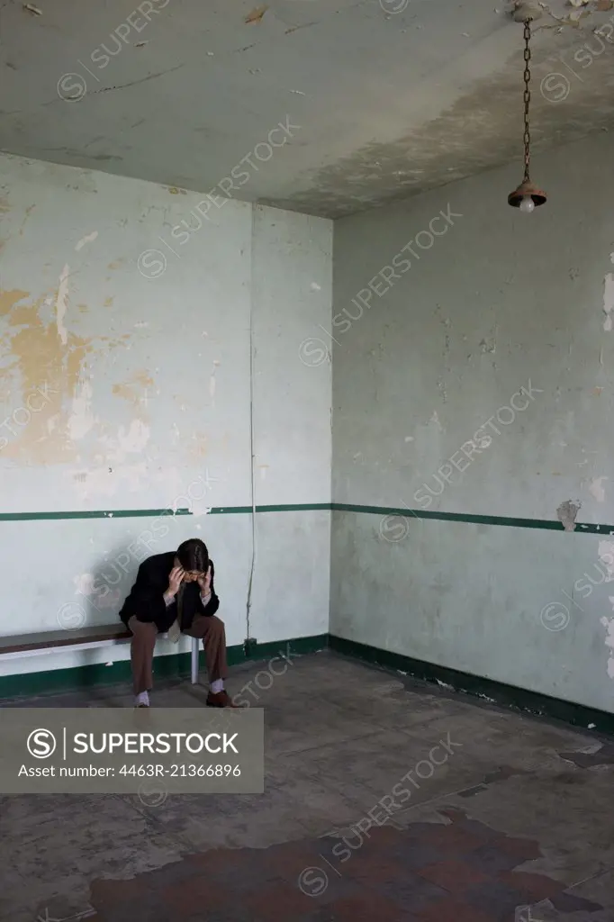 Young adult businessman sitting on a bench with his head in his hands in a derelict building.