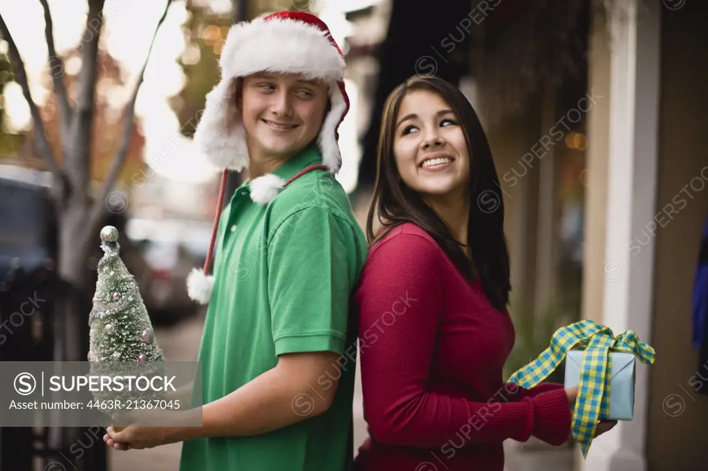 Teenage couple holding a miniature Christmas tree and a gift
