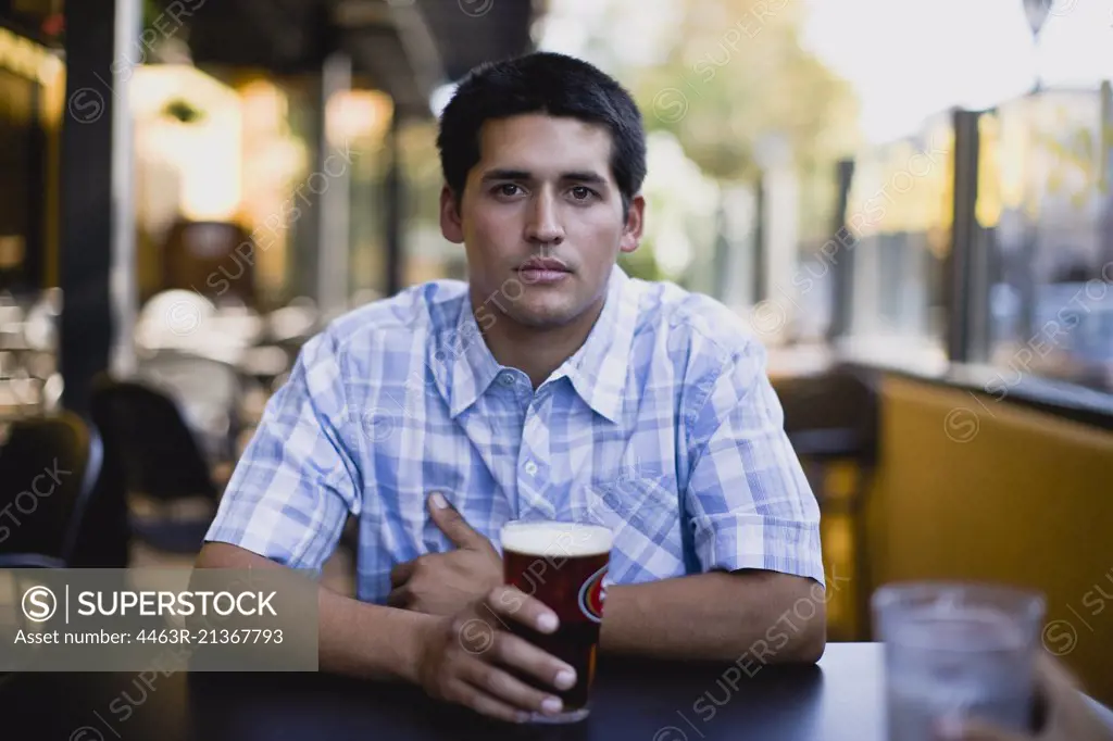 Portrait of a young adult man sitting at a bar having a beer.